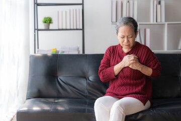 Asian elderly woman with heart disease feeling pain sitting on sofa at home