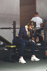 Fototapeta na wymiar Woman doing biceps curl with dumbbells in seated position. wearing blue leggins and long sleeve top.
