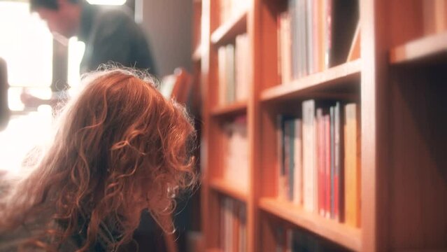 Little blonde girl choses a book to pick from the book shelf in the library