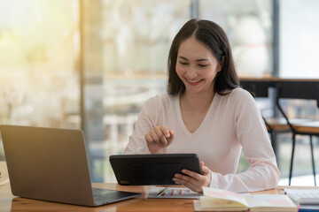 An Asian businesswoman using a digital tablet while sitting at a work desk in an office