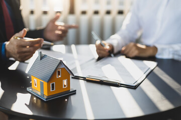 Businessman in suit in his office showing home insurance policy and pointing with a pen where the policyholder must to sign. Insurance agent consulting real estate insurance detail to customer.