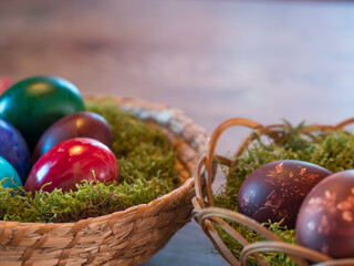 Various coloured decorated easter eggs in wicker basket nest with moss and colored Easter eggs on beige wooden bokeh background. For Happy Easter holiday card. Selective focus, copy space