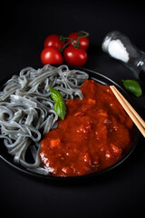 Black pasta with tomato sauce. On a black background. delicious