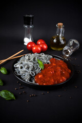 Black pasta with tomato sauce. On a black background. delicious