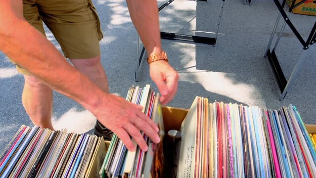 flea market flip in the city, man choosing vinyl records, antiques, old furniture, tables, used things, clothes and other goods are sold on street, recycling of unwanted items, pollution of nature