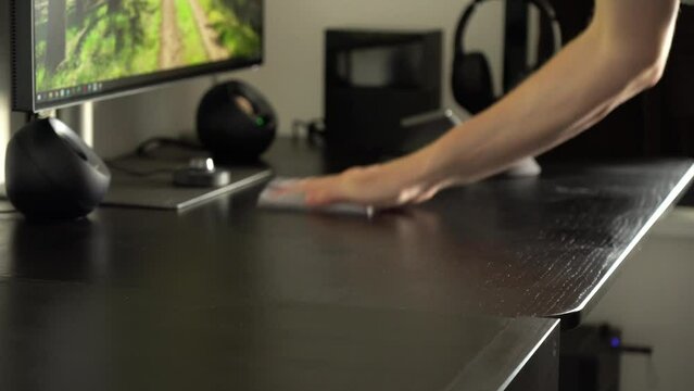 A man wipes an office table with a cloth and cleans under his computer setup - closeup