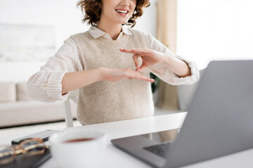 cropped view of cheerful teacher showing sign language gesture during online lesson on laptop.