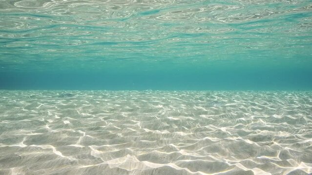Sandy shallow water in sunburst and glare on seabed sand, slow motion. Sunlight passes through surface of turquoise water and glares on sandy bottom in shallow water on bright sunny day