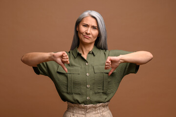 Upset disappointed asian middle age woman showing double thumbs down, refusing, criticizing with dislike gesture, disapproval, leaving bad review - obrazy, fototapety, plakaty