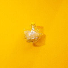 Close-up of crumpled plastic bottle isolated on yellow background.