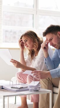 Shocked Young Couple Sitting On Sofa Looking At Bill