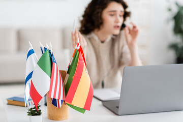 selective focus of different international flags near laptop and blurred language teacher working...
