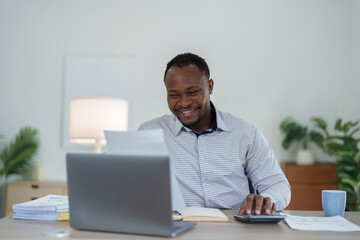 middle age man American African using calculator for calculating and laptop computer with planning working on financial document, tax, exchange, accounting and Financial advisor