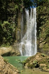 The idyllic Camugao Waterfall in Siquijor in the Philippines that flow into a natural pool of water surrounded by the light-lit rainforest.