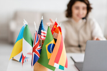 selective focus of various international flags near blurred laptop and language teacher having...