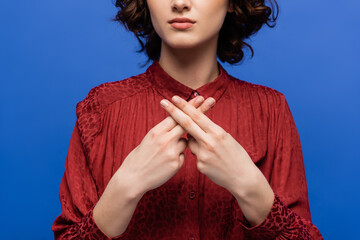 cropped view of young woman in red blouse teaching sign language isolated on blue.