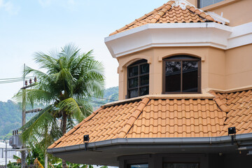 House with red clay tiled roof and gable and valley type of roof construction. House with a new roof made of orange metal. Corrugated metal roof and metal roofing.