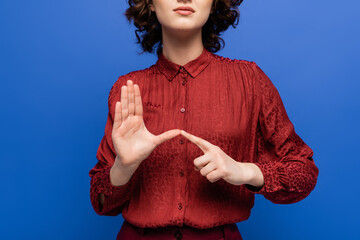 partial view of teacher in burgundy blouse using sign language isolated on blue.