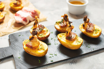 Golden potato halves baked with bacon served on a black board.