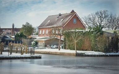 Fototapeta na wymiar Piękna śnieżna zima w Niderlandach. Spokojny wiejski krajobraz z wiejskim domem i kanałem.