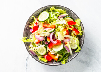 Vegan salad with green leaves, cucumber and bell pepper on white. Top view with copy space.