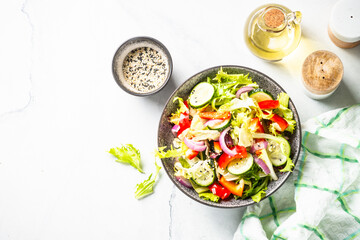 Fresh vegetable salad with green leaves, cucumber and bell pepper on white. Top view with copy space.