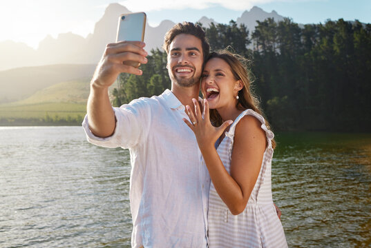 Couple, nature selfie and engagement by lake for celebration, happiness and excited for future. Man, woman and photography for social media, profile picture and romance with love, proposal and goals