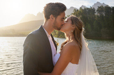 Love, wedding and a newlywed couple kissing by a lake outdoor in celebration of their marriage for romance. Water, summer or kiss with a bride and groom bonding together in tradition after ceremony