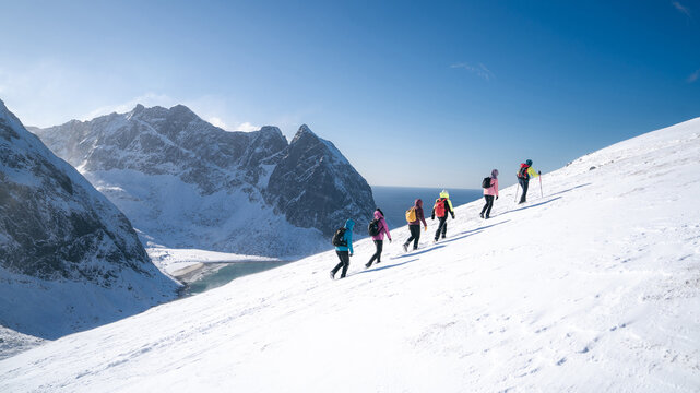 Process of hiking in Northern Norway, Lofoten Islands, Nordland, on the way to Ryten mountain and Kvalvika beach, with a groups of hikers, and mountains around, sunny winter day