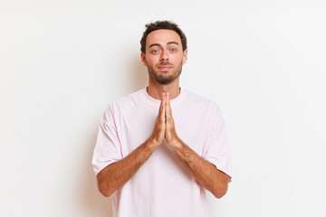 Young handsome man with beard wearing casual t-shirt standing over white background praying with hands together asking for forgiveness 