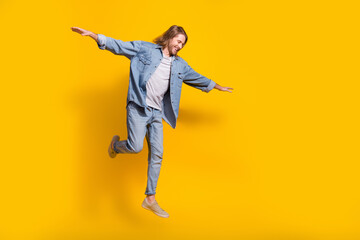 Fototapeta na wymiar Full length photo of cool cheerful guy dressed jeans shirt jumping high emtpy space isolated yellow color background