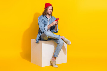 Full length photo of positive cool guy dressed jeans shirt texting device empty space isolated yellow color background