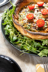 Vertical view of a vegetarian homemade Quiche with tomatoes, spinach, sweet pepper and cheese on black plate.