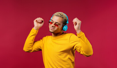 Positive man listening music, enjoying dance with headphones on crimson studio