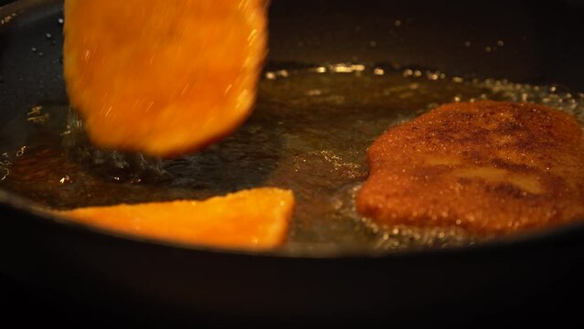 Chicken schnitzels frying on a pan are turned over - closeup
