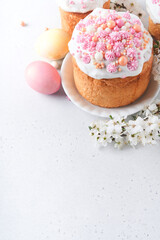 Traditional Easter sweet bread or cakes with white icing and sugar decor, colored eggs and cherry blossom tree branch over white table. Various Spring Easter cakes. Happy Easter day. Selective focus.