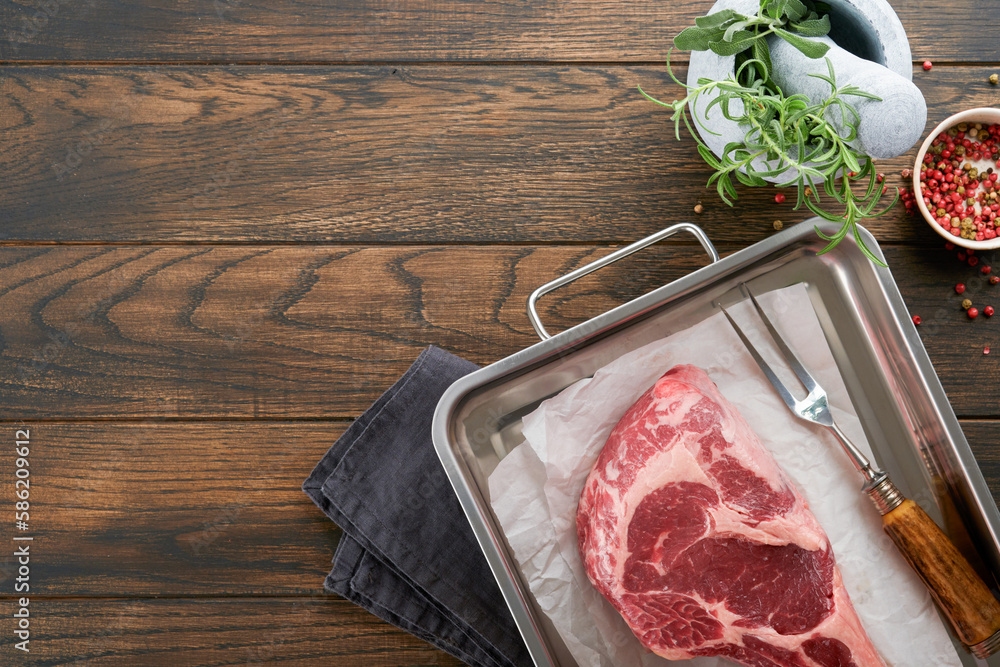 Wall mural Fresh tomahawk raw steak. Dry aged raw tomahawk beef steak with herbs and salt on old wooden background. Preparing to grill.  Top view and copy space.