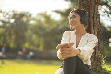 Portrait of smiling beauty asian woman happy and relax listening to music with headphones and singing, happy calm, resting ,good healthy, podcast, sound audio, listen online song at green park