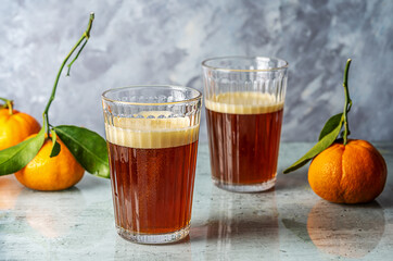 Chinotto refreshing drink in two glass on a grey glass surface with citrus fruits and gray background