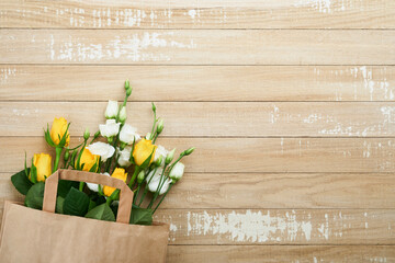Easter concept. Bouquet of fresh white and yellow roses in paper bag on old wooden background. Passover Pesah celebration concept. Concept of mothers day, womens day, spring background. Top view