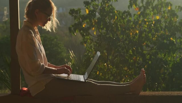Pretty blonde woman using laptop while sitting on the rooftop in sunlight. Remotely working concept.