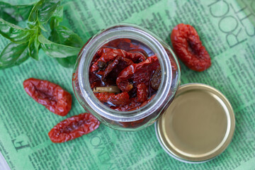 Dried tomatoes in a jar surrounded by ingredients and basil for cooking. Rustic style, top view.