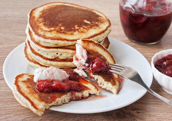 A stack of delicious sweet and spicy American pancakes with strawberry jam and sour cream on a white plate. Breakfast.