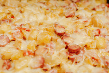 Rustic baked potatoes in the oven close-up. Melted cheese on top. Tomatoes, sausages, garlic, mayonnaise, pepper, spices in the recipe. Selective focus