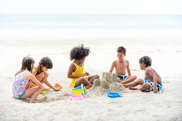 Obraz premium Group of Diversity little child boy and girl friends playing beach toy and build a sand castle together at tropical beach. Children kids enjoy and fun outdoor lifestyle travel ocean on summer vacation
