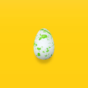 Outstanding white egg with green paint on a pastel yellow background.