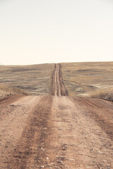 A dirt road leading off into the distance and over a distant hill on the horizon under a clear blue sky.
