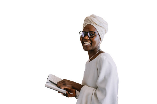 Cheerful African young woman in white turban, glasses and white dress holds diary, pen standing at home against transparent background looks at camera smiles. student female remote learning. Education