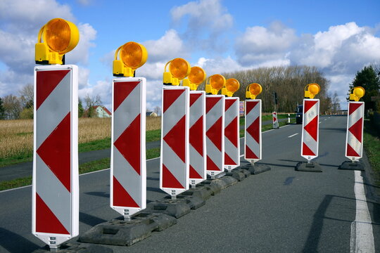 Warnbaken mit Streifen in Rot und Weiß und Blinkleuchten in Gelb an einer Baustelle mit Absperrung an der Landstraße in Lage bei Detmold in Ostwestfalen-Lippe