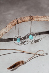 Handmade jewelry earrings made of natural turquoise and Silver on stone and modern concrete background with snag and dry flower
